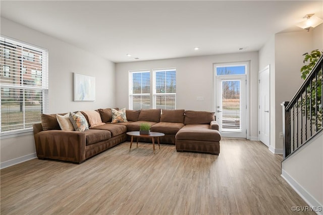 living area featuring baseboards, stairway, light wood-style flooring, and a healthy amount of sunlight