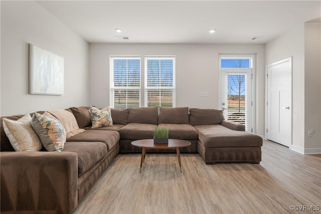 living room with light wood-type flooring, visible vents, and baseboards