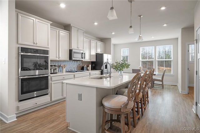 kitchen featuring a kitchen island with sink, stainless steel appliances, a sink, light countertops, and tasteful backsplash