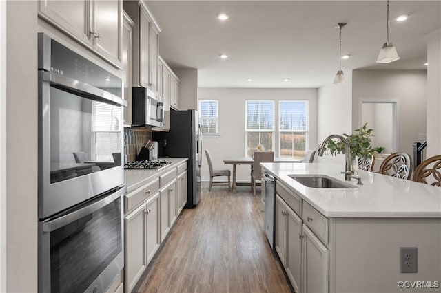 kitchen featuring tasteful backsplash, an island with sink, stainless steel appliances, light countertops, and a sink