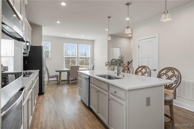 kitchen with a center island with sink, a breakfast bar area, appliances with stainless steel finishes, wood finished floors, and a sink