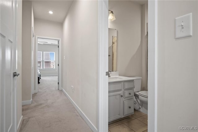 hallway featuring light carpet, light tile patterned flooring, a sink, and baseboards