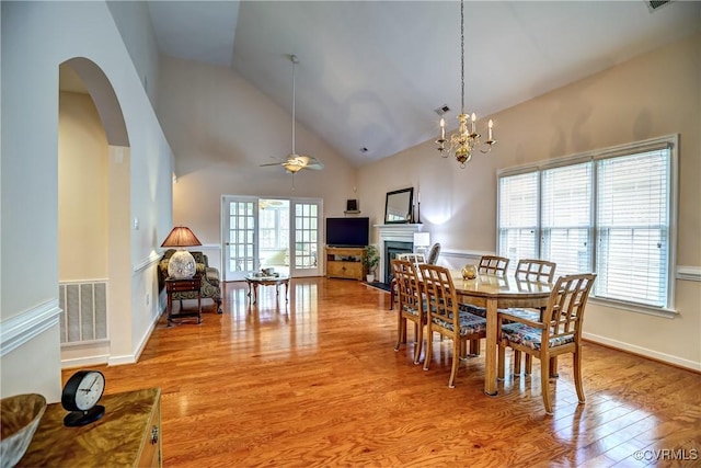 dining area featuring arched walkways, a fireplace, visible vents, high vaulted ceiling, and light wood-type flooring