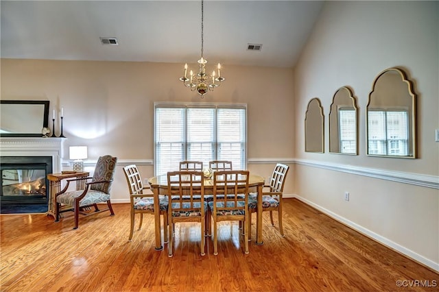 dining space featuring visible vents, a multi sided fireplace, vaulted ceiling, wood finished floors, and baseboards