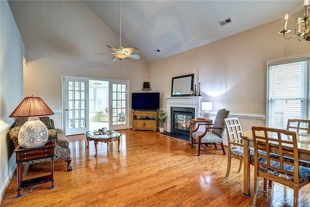 interior space with high vaulted ceiling, light wood-style flooring, ceiling fan with notable chandelier, a fireplace with flush hearth, and visible vents