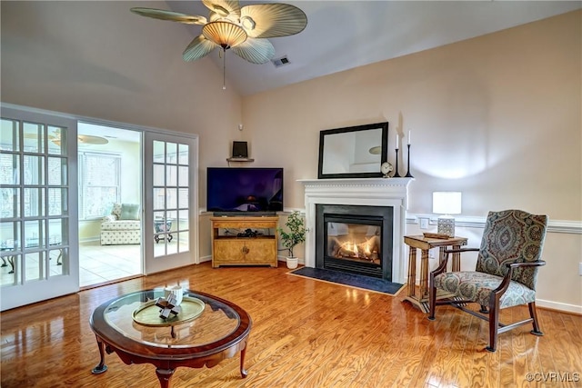 living room with visible vents, a ceiling fan, a fireplace with flush hearth, wood finished floors, and vaulted ceiling