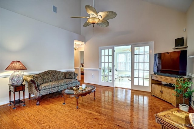 living area with visible vents, a high ceiling, a ceiling fan, and wood finished floors