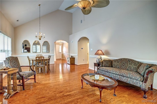 living area with arched walkways, high vaulted ceiling, ceiling fan with notable chandelier, and wood finished floors