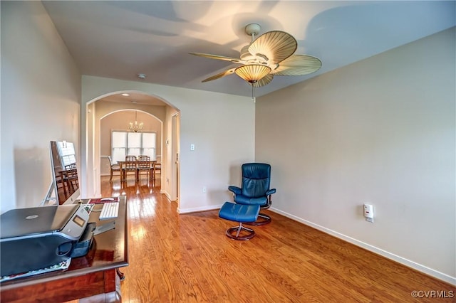 sitting room with arched walkways, ceiling fan with notable chandelier, wood finished floors, and baseboards