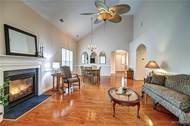 living area with arched walkways, visible vents, a fireplace with flush hearth, wood finished floors, and ceiling fan with notable chandelier