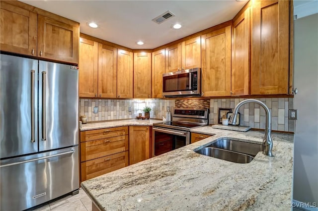 kitchen featuring visible vents, appliances with stainless steel finishes, light stone counters, a sink, and backsplash