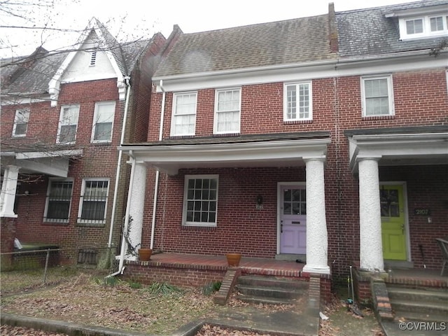 multi unit property featuring covered porch, brick siding, and fence