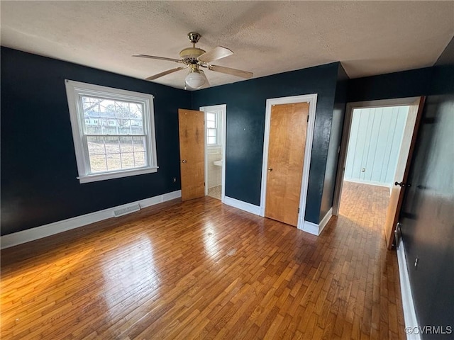 unfurnished bedroom with a textured ceiling, hardwood / wood-style flooring, visible vents, and baseboards