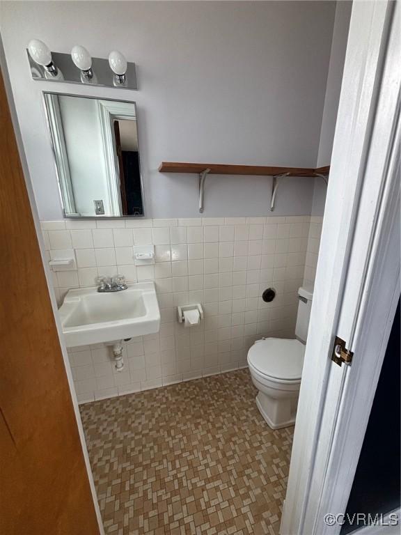 half bathroom featuring toilet, tile walls, a sink, and wainscoting