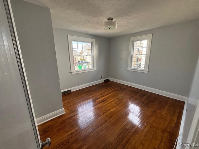 unfurnished room with visible vents, dark wood-style floors, a wealth of natural light, and baseboards