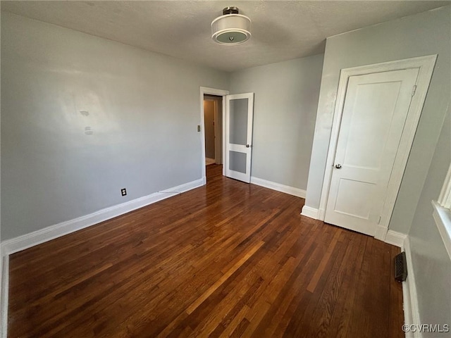 unfurnished bedroom with dark wood-style flooring, a textured ceiling, and baseboards