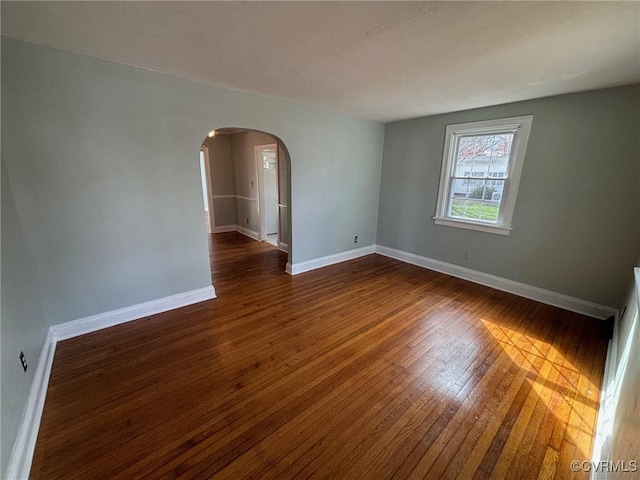 empty room featuring arched walkways, dark wood finished floors, and baseboards