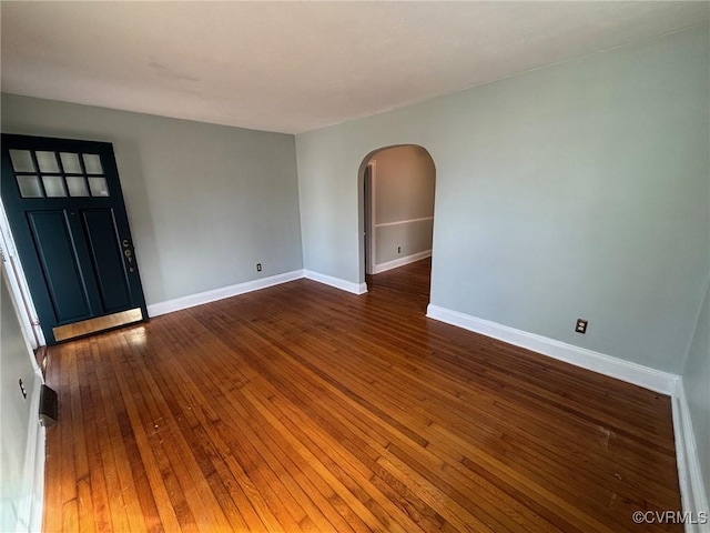 unfurnished room with arched walkways, dark wood finished floors, and baseboards