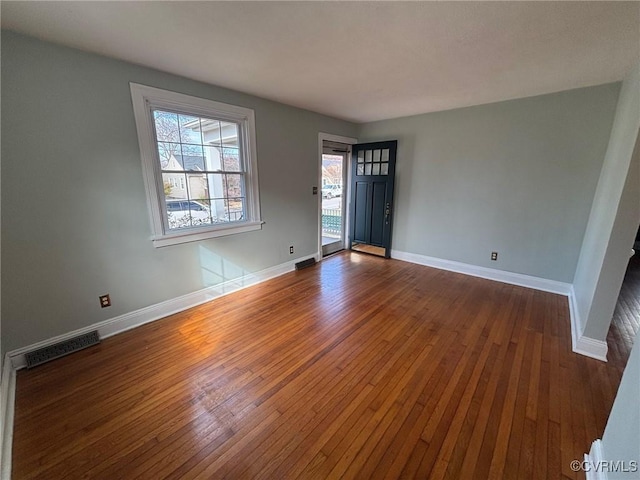 spare room with dark wood-style flooring, visible vents, and baseboards