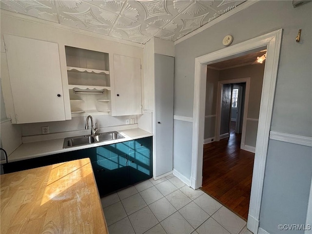 kitchen featuring baseboards, an ornate ceiling, light countertops, open shelves, and a sink