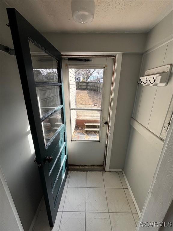 doorway to outside with baseboards, a textured ceiling, and light tile patterned flooring