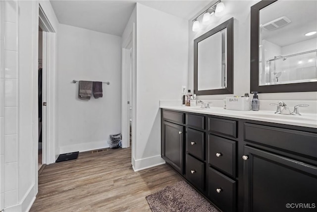 bathroom with a sink, wood finished floors, visible vents, double vanity, and walk in shower