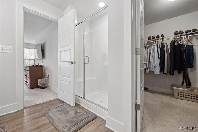 full bath featuring a walk in closet, a shower stall, baseboards, and wood finished floors