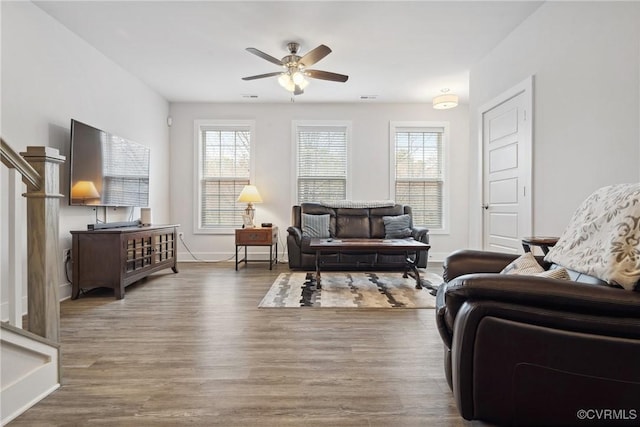 living room featuring ceiling fan, wood finished floors, visible vents, baseboards, and stairs