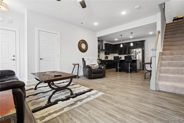 living area with recessed lighting, a ceiling fan, baseboards, light wood-style floors, and stairway