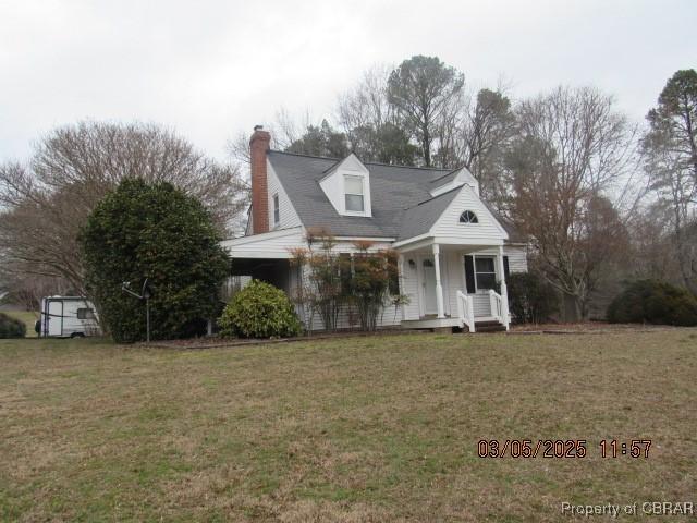 new england style home featuring covered porch, a chimney, and a front lawn