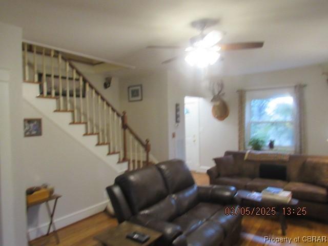 living area with wood finished floors, ceiling fan, baseboards, and stairs