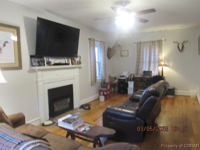 living area with ceiling fan, a fireplace, baseboards, and wood finished floors