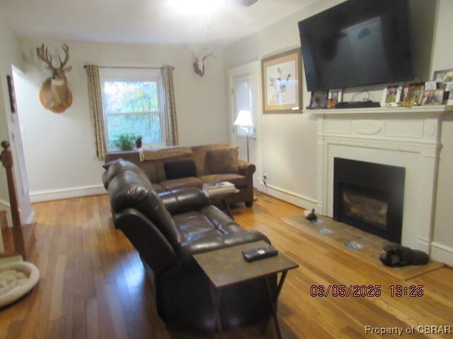 living area featuring a ceiling fan, baseboards, wood finished floors, and a glass covered fireplace