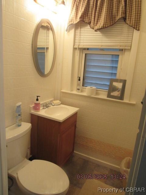 bathroom featuring vanity, toilet, and tile walls