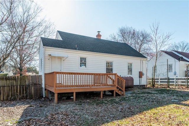 back of house with a chimney, a shingled roof, a wooden deck, a fenced backyard, and heating fuel