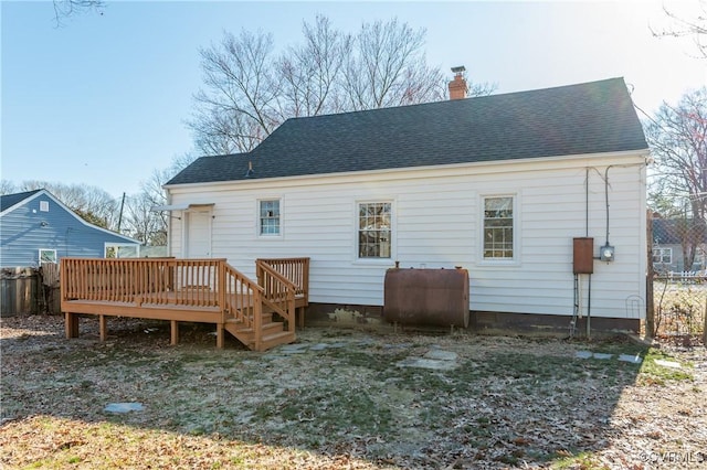 rear view of property with a chimney, a shingled roof, fence, a deck, and heating fuel