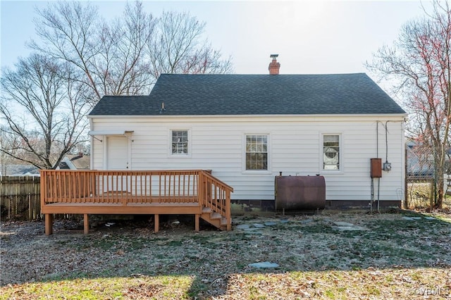 back of house with fence, roof with shingles, a wooden deck, heating fuel, and a chimney