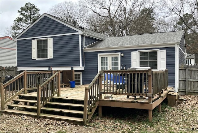 rear view of house with fence, a deck, and roof with shingles