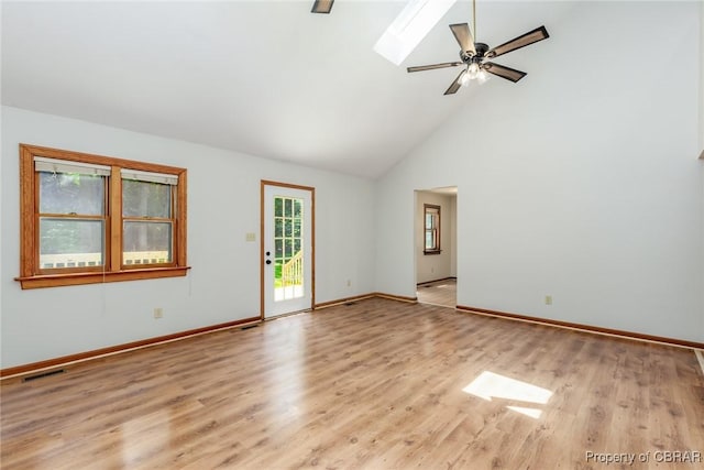 empty room with a skylight, visible vents, baseboards, light wood-style flooring, and high vaulted ceiling
