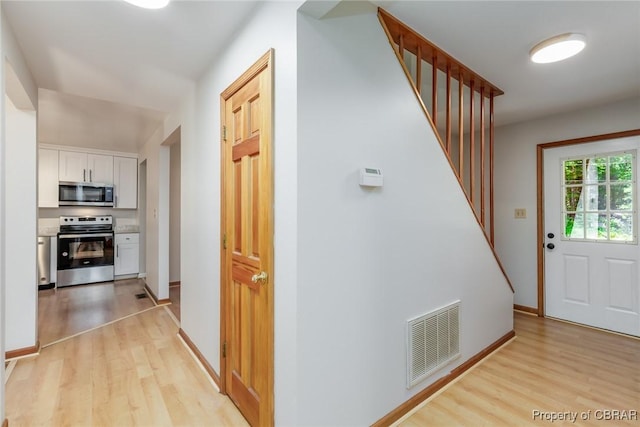 hallway with light wood-type flooring, stairway, baseboards, and visible vents