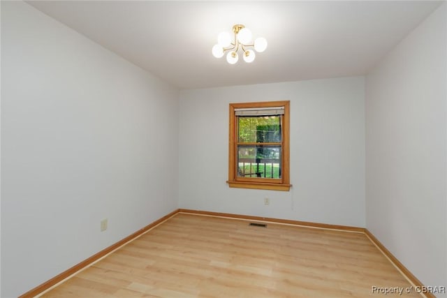 spare room featuring baseboards, a chandelier, visible vents, and light wood-style floors