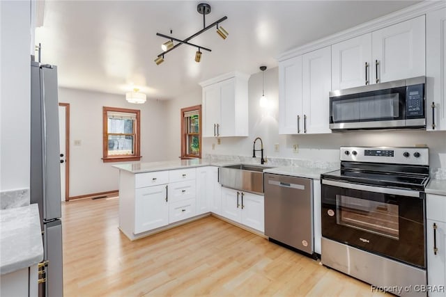 kitchen with a peninsula, a sink, white cabinetry, appliances with stainless steel finishes, and light wood-type flooring