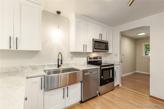 kitchen with hanging light fixtures, appliances with stainless steel finishes, light wood-style floors, white cabinetry, and a sink