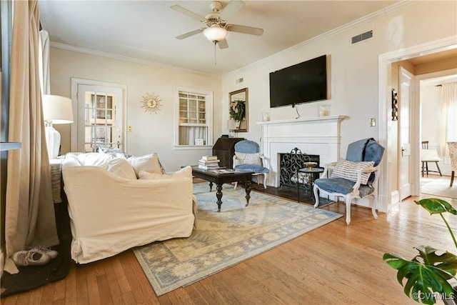 living area featuring a fireplace, visible vents, ornamental molding, ceiling fan, and wood finished floors