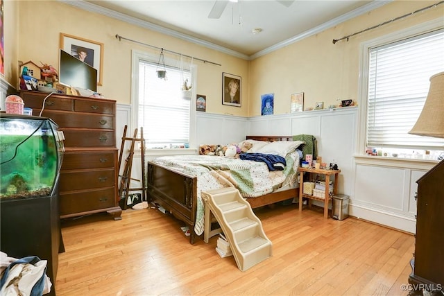 bedroom featuring ornamental molding, light wood-type flooring, wainscoting, and a decorative wall