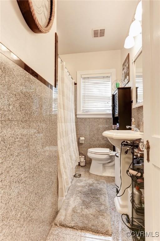 full bathroom featuring tile walls, visible vents, toilet, wainscoting, and a sink