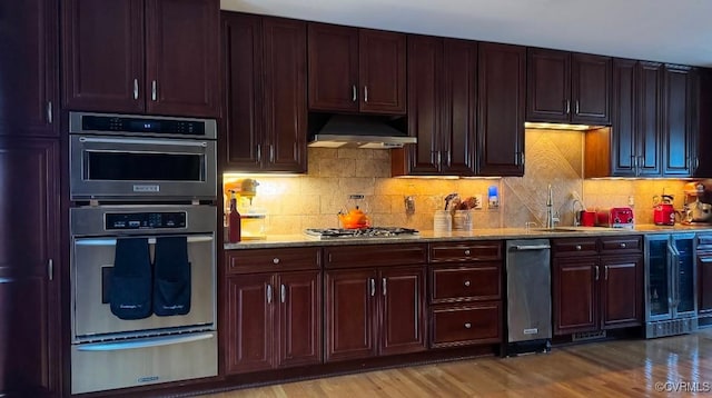 kitchen featuring light wood-style flooring, stainless steel appliances, under cabinet range hood, a sink, and a warming drawer