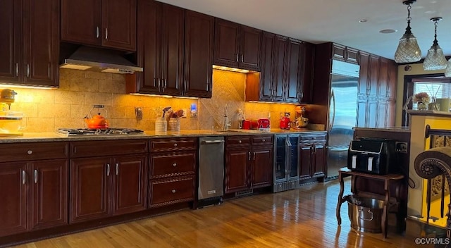 kitchen featuring appliances with stainless steel finishes, wood finished floors, decorative light fixtures, and under cabinet range hood