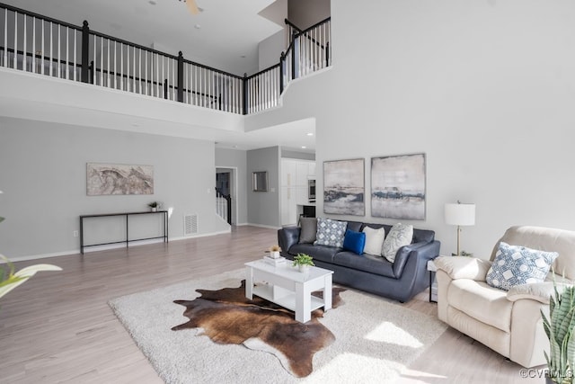 living area with visible vents, stairway, a high ceiling, wood finished floors, and baseboards