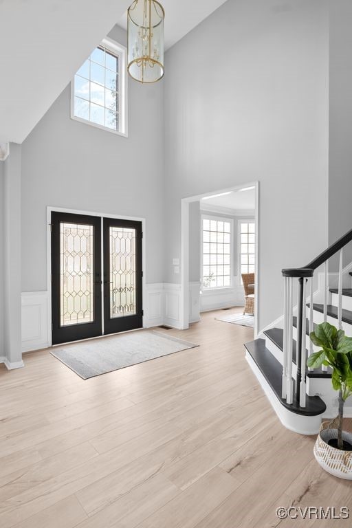 entryway with stairway, wood finished floors, an inviting chandelier, french doors, and a decorative wall